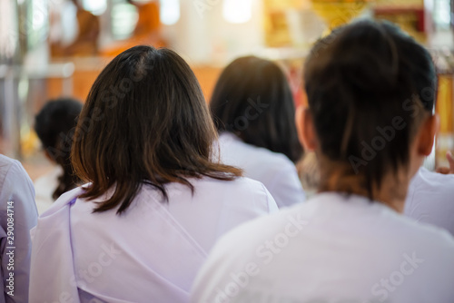 A group of Asian Buddhist women wearing white dresses, sit in the temple to observe eight Buddhist precepts for practices Dharma in the Buddhist holy day.