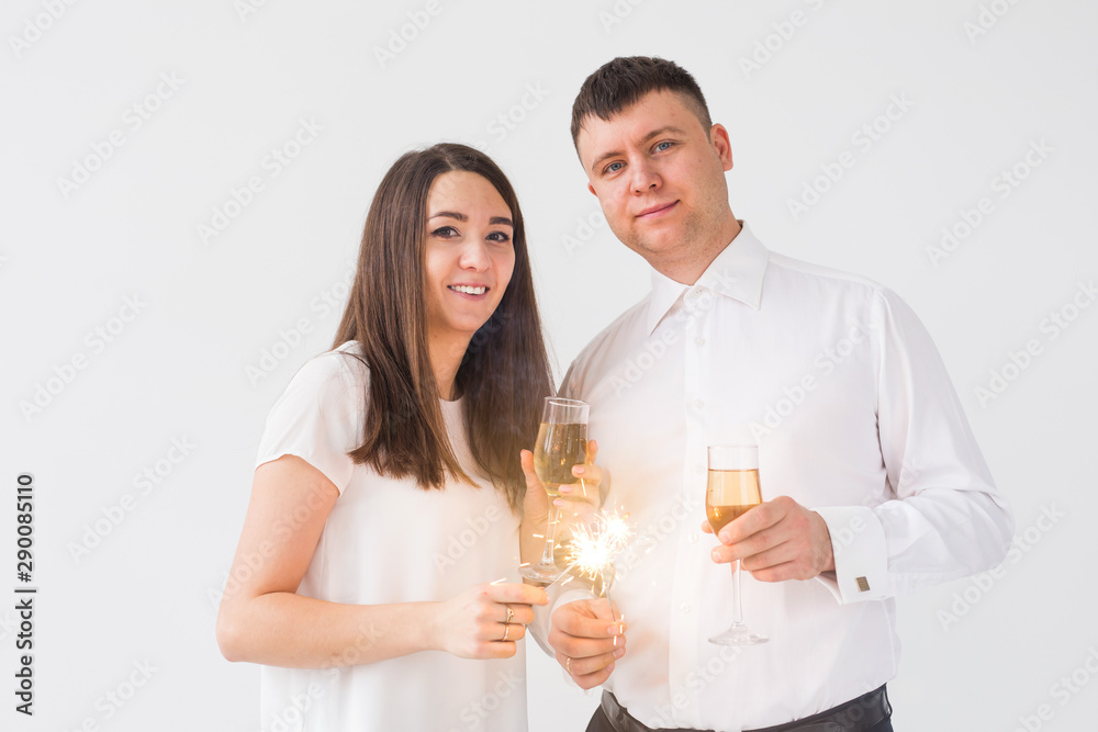 New year, holidays, date and valentines day concept - Loving couple holding sparklers light and glasses of champagne over white background New year, holidays, date and valentines day concept - Loving couple holding sparklers light and glasses of champagne over white background