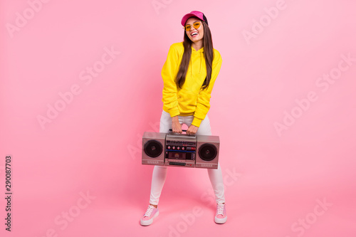 Full length body size photo of cheerful charming cute cap nice pretty sweet gorgeous woman holding old sound cassette recorder wearing yellow sweater isolated over pink pastel color background