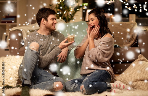 christmas, holidays and people concept - happy couple with gift box at home over snow