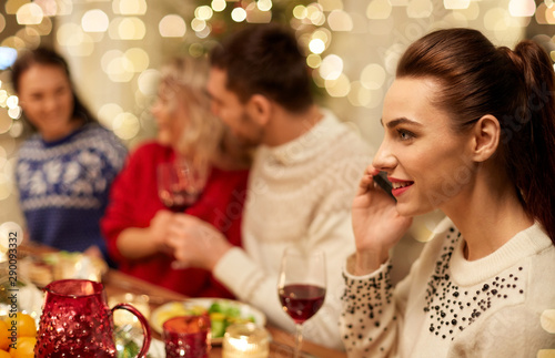 holidays  communication and celebration concept - close up of young woman calling on smartphone and having christmas dinner with friends at home