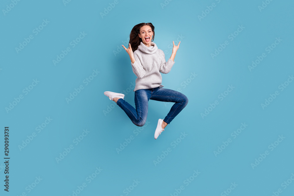 Full length photo of excited cheerful girl show horns sign jump have fun visit concert scream wear white knitted pullover sweater denim jeans sneakers isolated over blue color background Full length photo of excited cheerful girl show horns sign jump have fun visit concert scream wear white knitted pullover sweater denim jeans sneakers isolated over blue color background
