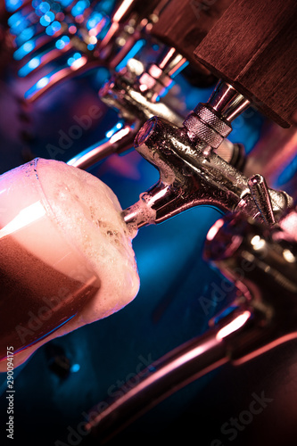 Bartender pouring a large lager beer in tap. Bright and modern neon light  males hands. Pouring beer for client. Side view of young bartender pouring beer while standing at the bar counter.