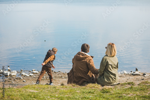 family walking near water. sitting at the beach. little kid throwing rock in water