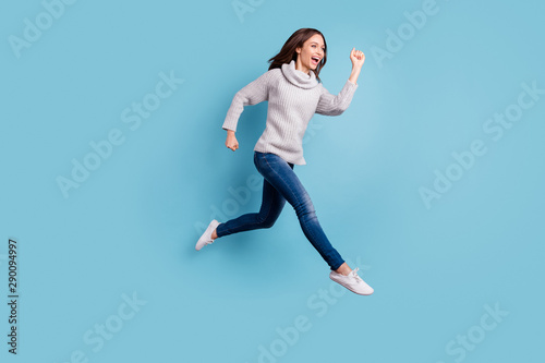 Full size profile side photo of excited candid teen run jump have free time wear knitted sweater pullover denim jeans sneakers isolated over blue color background