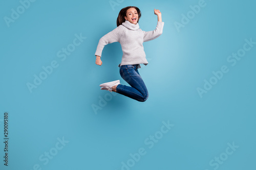 Full length photo of cute excited enthusiastic girl jump have free time enjoy vacation wear white sweater pullover denim jeans sneakers isolated over blue color background