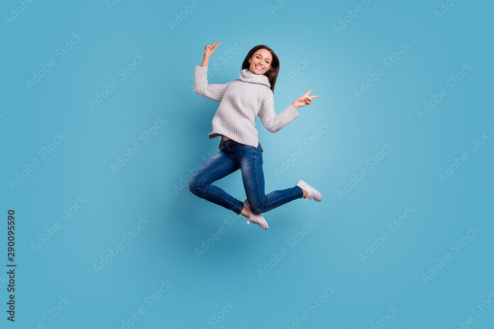 Portrait of content playful youth jump have free time make v-signs wear white knitted sweater pullover denim jeans sneakers isolated over blue color background Portrait of content playful youth jump have free time make v-signs wear white knitted sweater pullover denim jeans sneakers isolated over blue color background