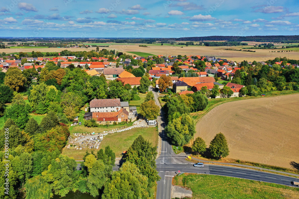 Aerial view of an intersection of country roads in front of the entrance to a small village in the flat landscape of Northern Germany