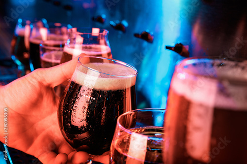 Hand of bartender pouring a large ale, porter, stout beer in tap. Bright and modern neon light, males hands. Pouring beer for client. Side view of young bartender pouring beer while standing at the photo