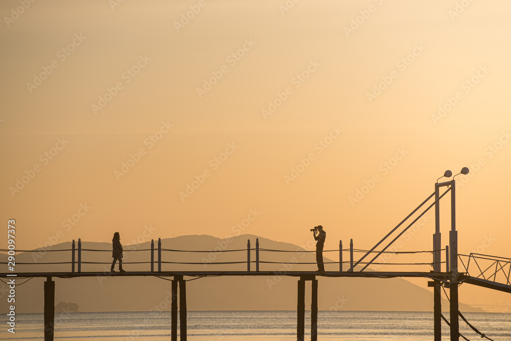 a silhouette of lovers taking pictures on the bridge over the sea of the sunset