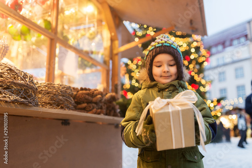 holidays, childhood and people concept - happy little boy with gift box at christmas market in winter evening