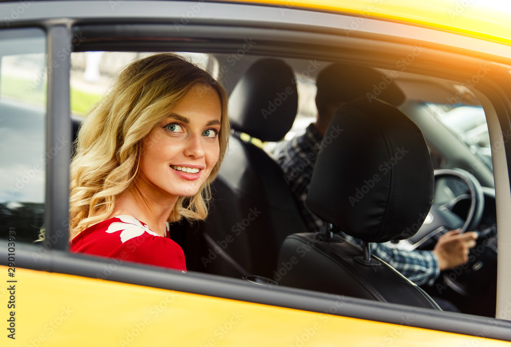 Photo of young woman sitting in back seat of yellow taxi in summer.