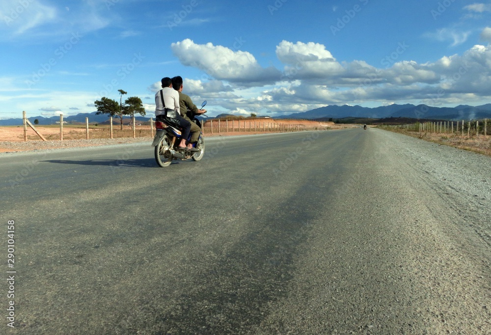 Two young people riding a motorcycle on a completely empty, recently built road in Laos.