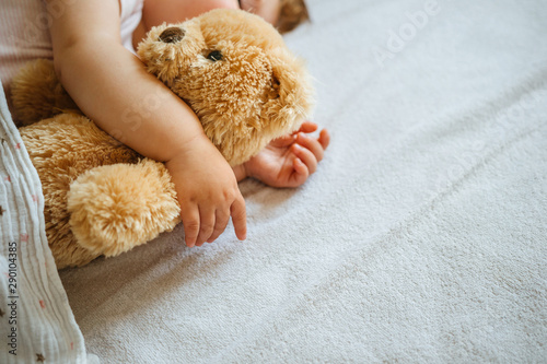Little baby sleeping and embracing soft toy bear, close-up on hands