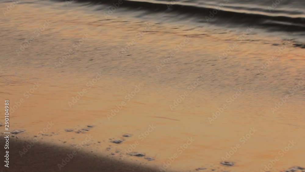 Subdued romantic warm iridescent colors reflecting off the soaking wet sand at sunset and waves overflowing the sand particles.