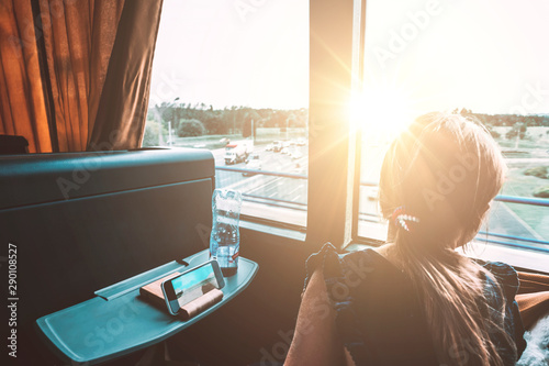 Young girl looking out bus window. Sunset landscape and road with cars. Peaceful single