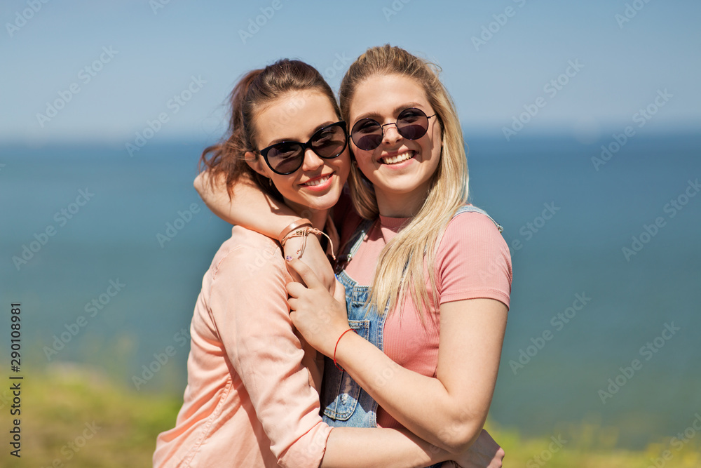 leisure and friendship concept - happy smiling teenage girls or best friends in sunglasses hugging at seaside in summer