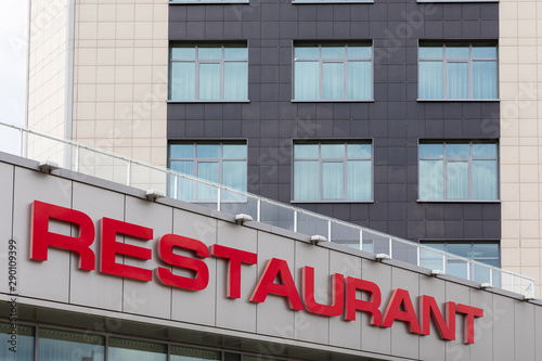 Red restaurant title on modern gray tiled building facade.