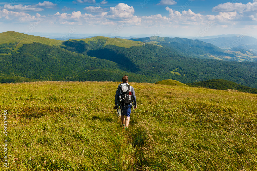 mężczyzna z plecakiem wędrujący po górach zielonych porośniętych trawą, widziany od tyłu
