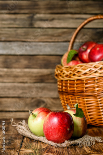 Red organic apples in a wicker basket on a wooden background.