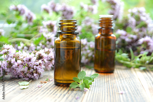 Essential oil of oregano in a bottle and fresh flowers on a wooden table Natural cosmetics and aromatherapy