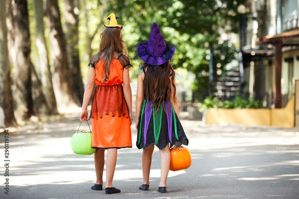 Young girls in halloween costumes with pumkin buckets walking on the street