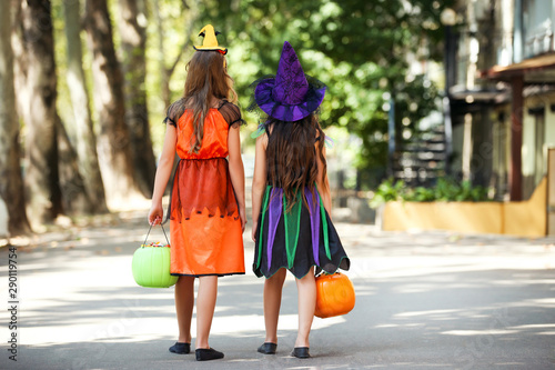 Young girls in halloween costumes with pumkin buckets walking on the street