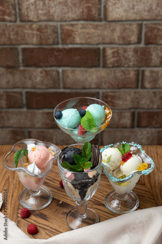 Different kinds of sundae ice cream desserts served on wooden table and brick background: vanilla sundae, strawberry ice cream dessert with whipped cream, oreo ice cream dessert and bubblegum sundae