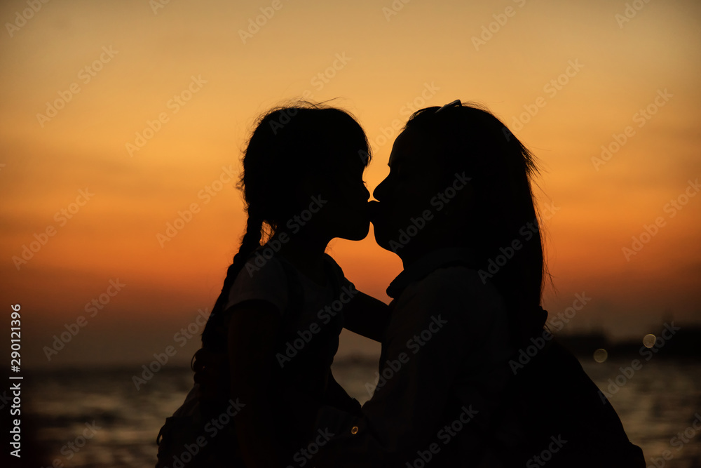Silhouette of a young mother lovingly kissing her little child daughter
