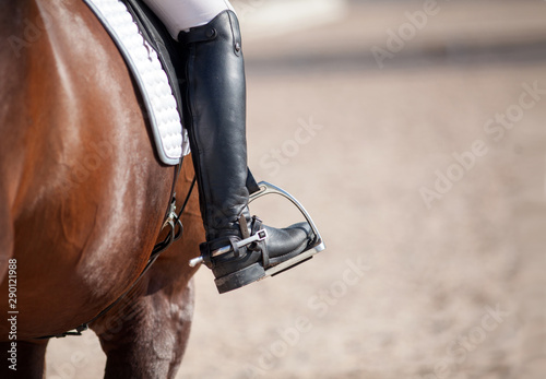 Croup of a red horse with a white saddle and a rider’s foot in a boot with a spur inserted in a stirrup. © Alexander