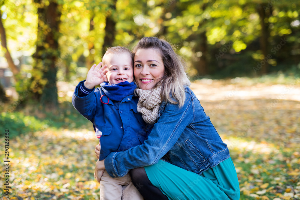 Young mother with small toddler son on a walk in autumn forest, resting.