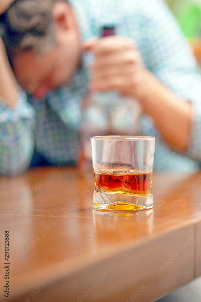 A glass of whiskey on the table on the background of a drunken man. Alcoholic father  