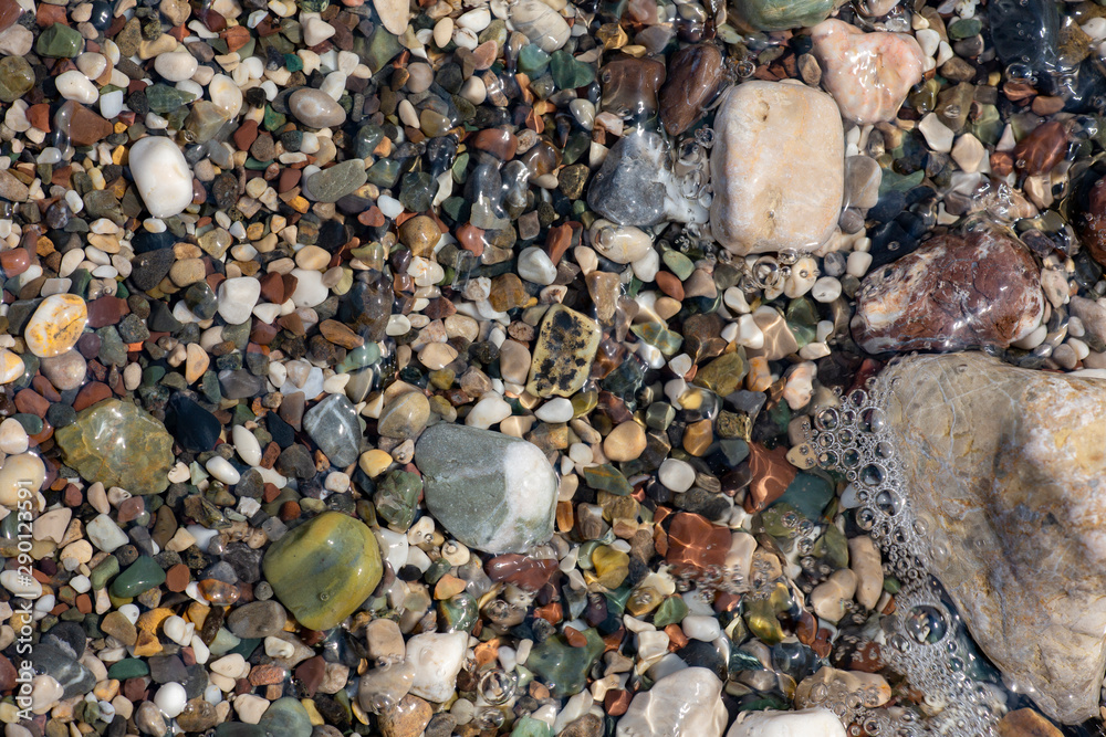 Thin white foam and the many small bubbles on the glittering sea water with the colorful pebbles underneath Thin white foam and the many small bubbles on the glittering sea water with the colorful pebbles underneath