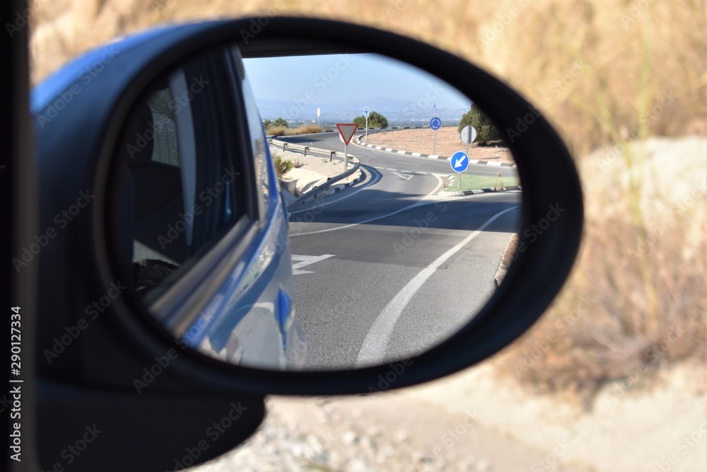 View of a roundabout, lanes and traffic signs in the rearview mirror of a vehicle
