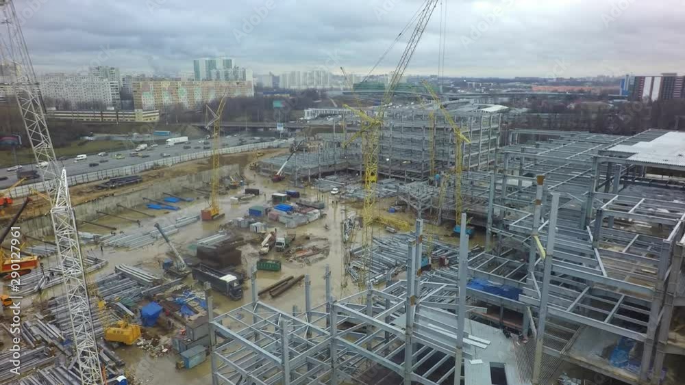 An aerial view of a large construction site full of construction cranes and multi storey building frames. The ground is covered with dirty puddles, construction elements and builders houses. Right An aerial view of a large construction site full of construction cranes and multi storey building frames. The ground is covered with dirty puddles, construction elements and builders houses. Right