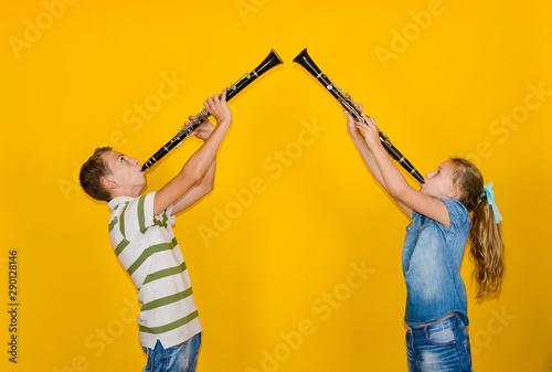 Valokuvatapetti A boy and a girl play the clarinet and stand against each other, on a yellow background