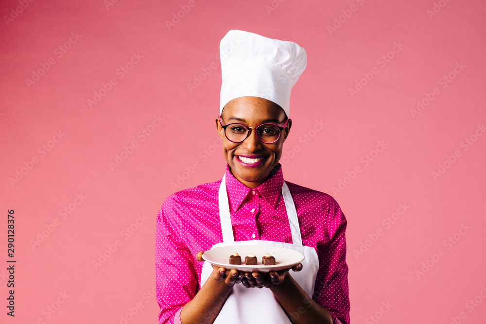 Portrait of a smiling young female chef holding a plate with three  chocolate pralines, isolated on pink studio background Stock Photo | Adobe  Stock