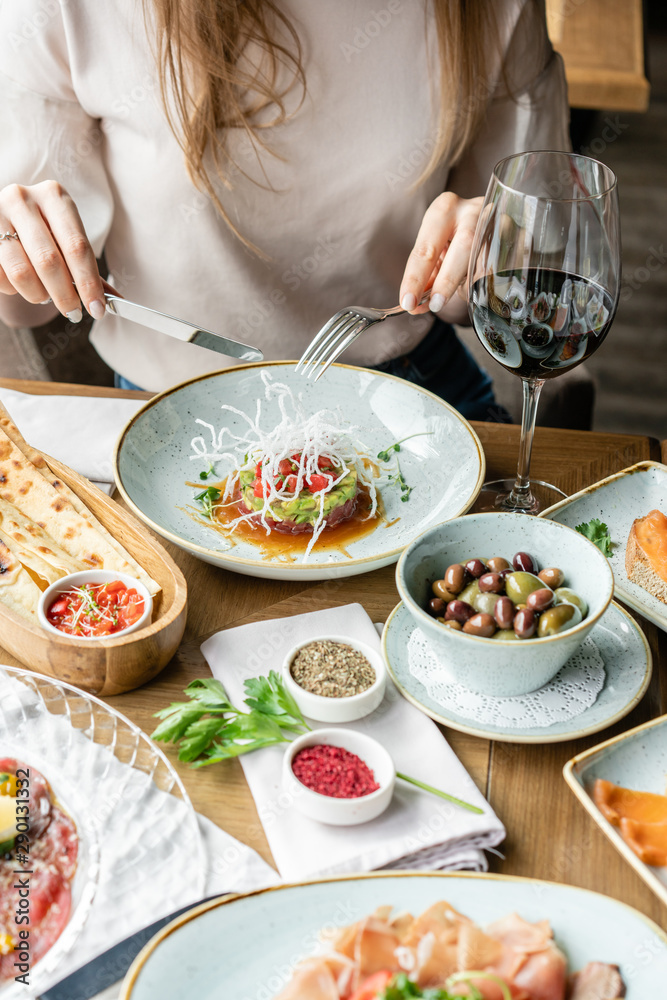 Closeup woman eating tartar in the restaurant. Variety of dishes on the table. Italian cuisine