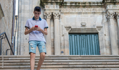 young teenage man with mobile phone walking in the city