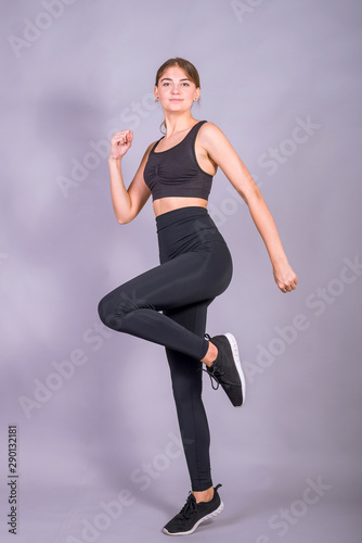 Young slim girl is jumping on a gray background. Photo of an active woman in sportswear.