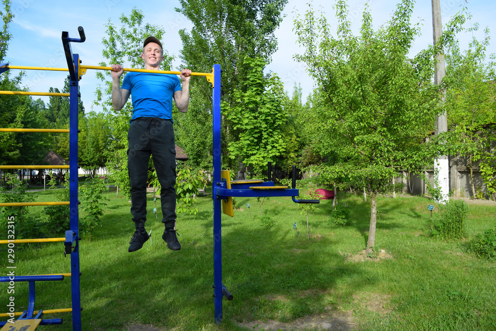Fototapeta premium A young man pulls up on a horizontal bar in the city Park.
