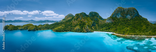 Aerial drone panoramic view of uninhabited tropical island with rugged mountains  rainforest jungle  sandy beaches surrounded by blue ocean