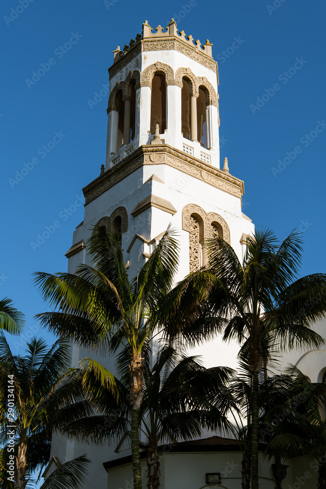 The setting sun highlights one side of a white bell tower and palm trees - Our Lady of Sorrows Church in Santa Barbara, California