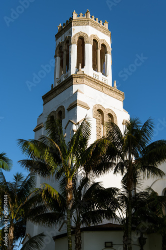 The setting sun highlights one side of a white bell tower and palm trees - Our Lady of Sorrows Church in Santa Barbara, California