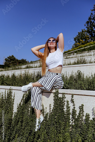 Girl with long hair in trendy striped trousers and in sunglasses and white sneakers