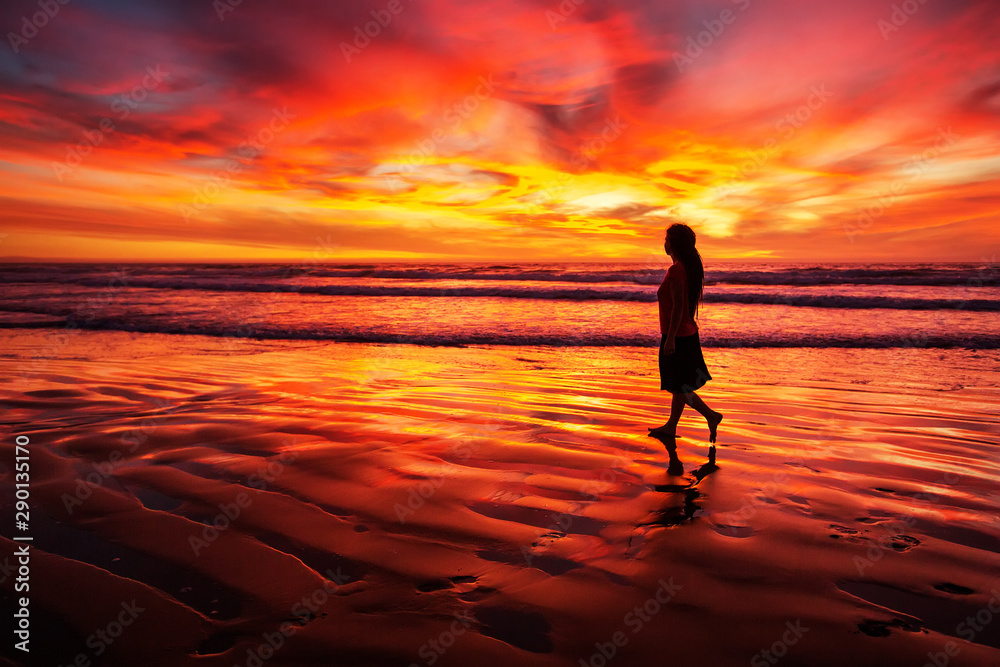 woman walking alone on the beach in the sunset