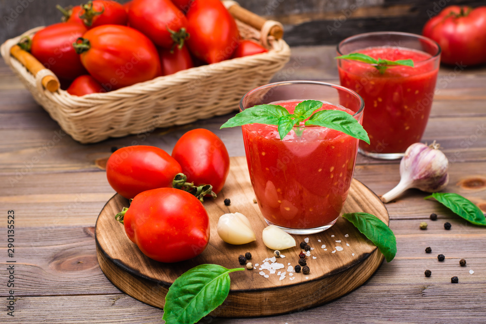 Fresh tomato juice with basil leaves in glasses and tomatoes on a wooden table Fresh tomato juice with basil leaves in glasses and tomatoes on a wooden table