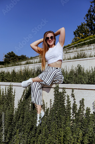 Girl with long hair in trendy striped trousers and in sunglasses and white sneakers