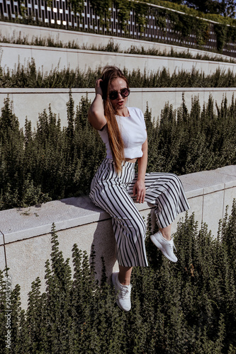 Girl with long hair in trendy striped trousers and in sunglasses and white sneakers