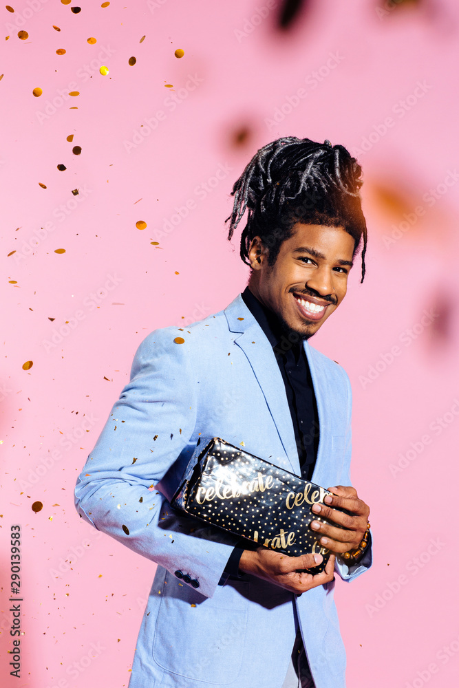 Man with gift smiling at camera with confetti falling on pink Man with gift smiling at camera with confetti falling on pink